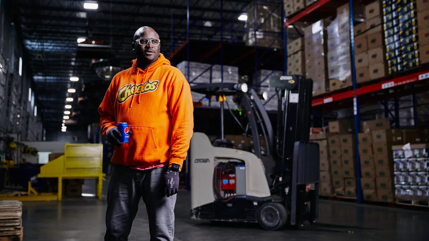 Man wearing Cheetos hoodie standing in a warehouse with boxes and a forklift in the background