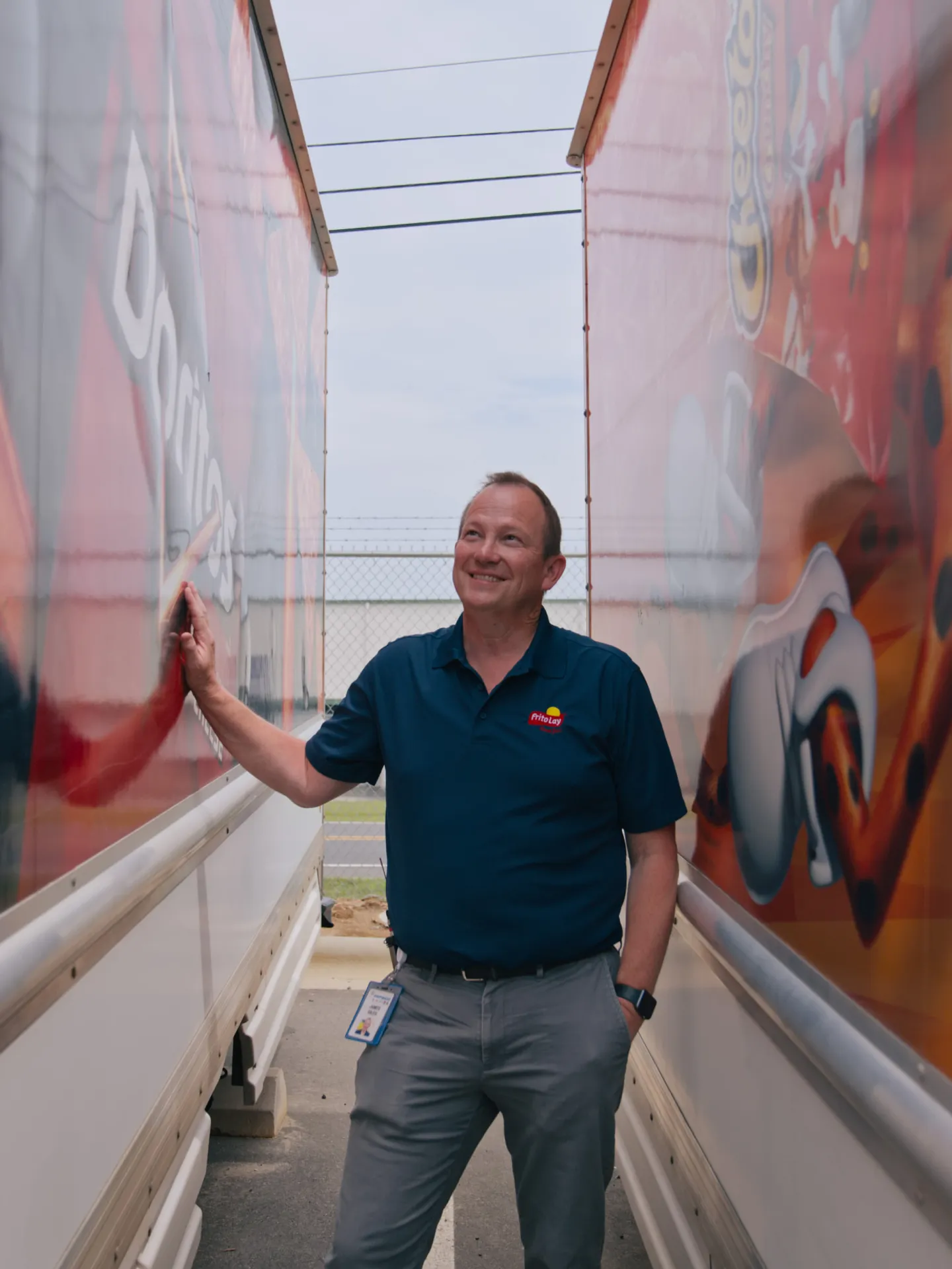Man in Frito-Lay uniform standing between a Cheetos truck and a Doritos truck
