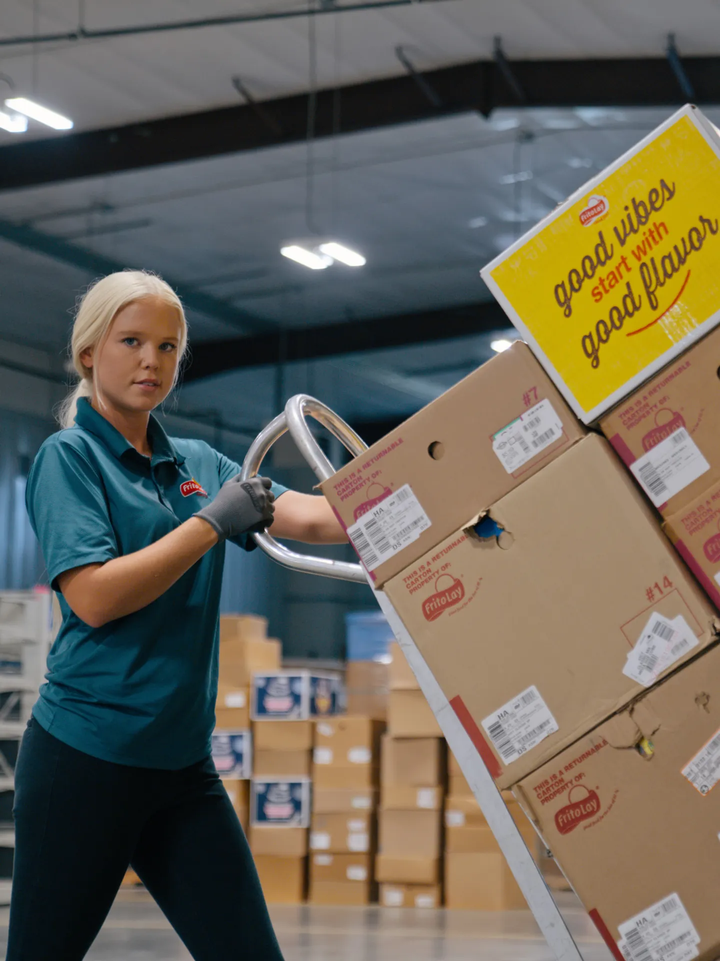Woman in a warehouse moving boxes of chips with a hand truck