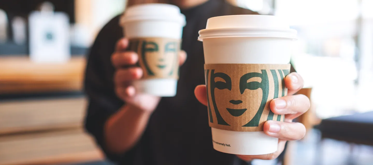 Person holding two coffee cups showing the Starbucks logo